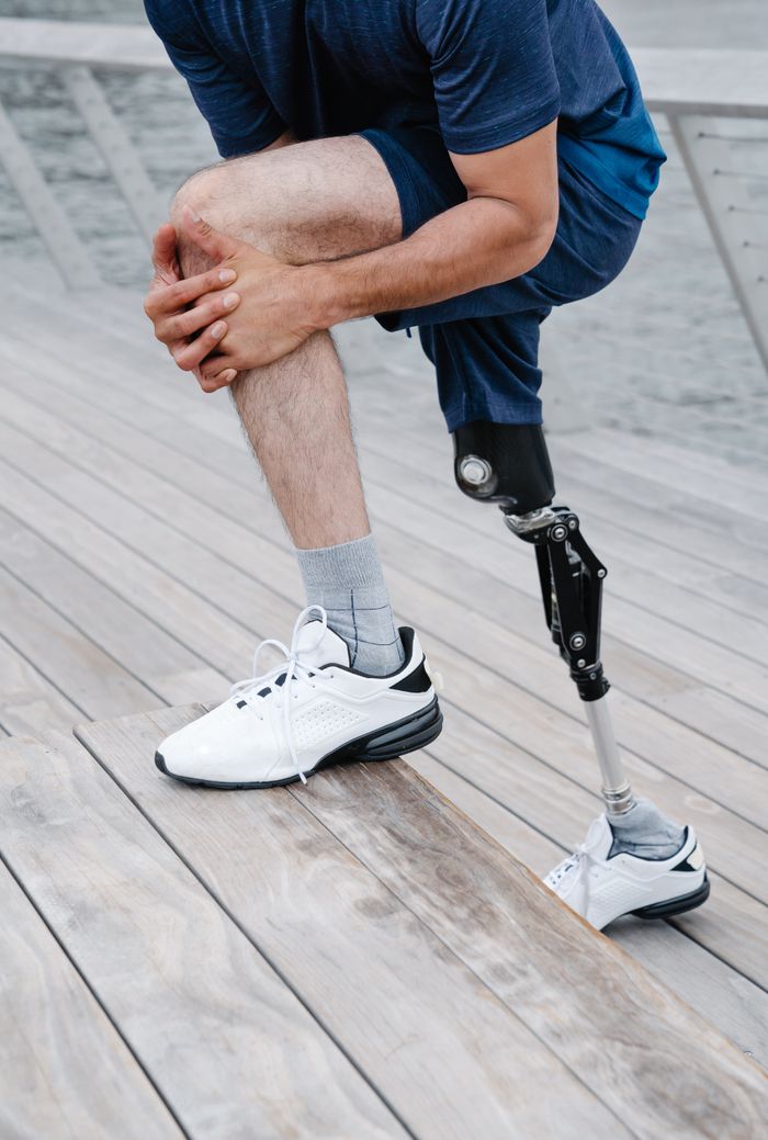 An adult male athlete with a prosthetic leg stretching on a wooden deck by the water.